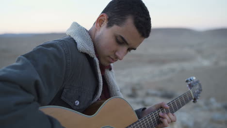 close up of young man playing guitar in the desert afternoon