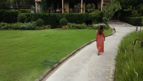 Beautiful-Lady-in-Red-Dress-Walking-Through-a-Botanical-Italian-Garden,-Aerial-Drone-Follow-Shot