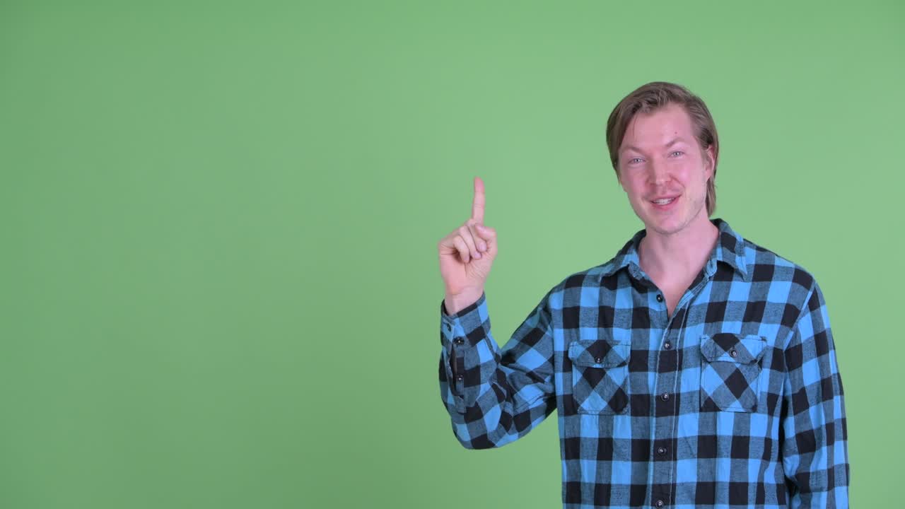 Portræt af kaukasisk mand, der smiler og peger mod kopiplads, filmet mod grøn studiebaggrund.
