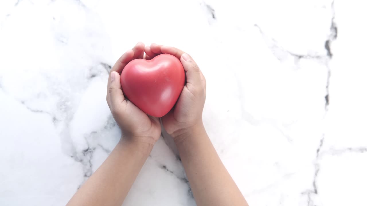 las manos del niño sosteniendo un corazón rojo