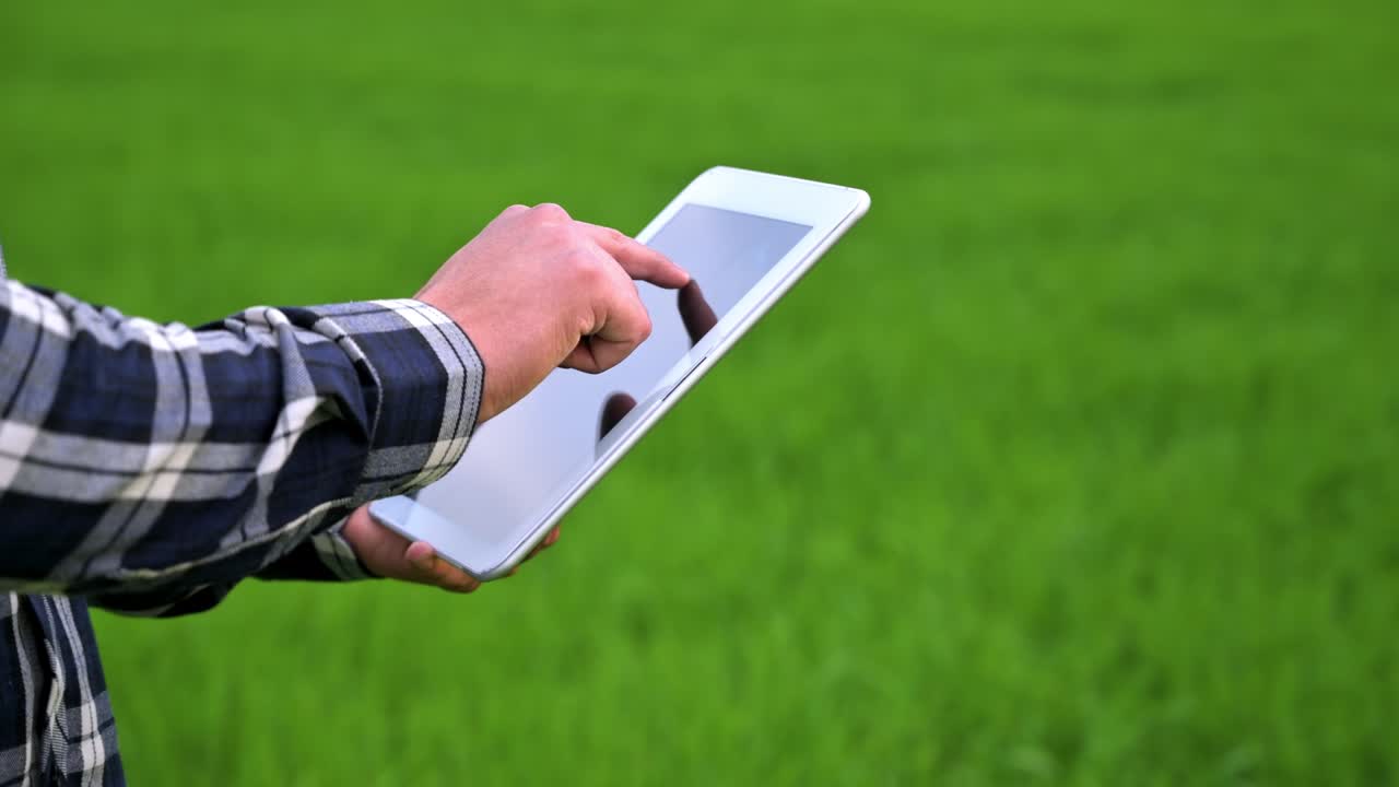 Close up of a Farmer man read or analysis a report in tablet computer on a green agriculture field. High quality 4k footage