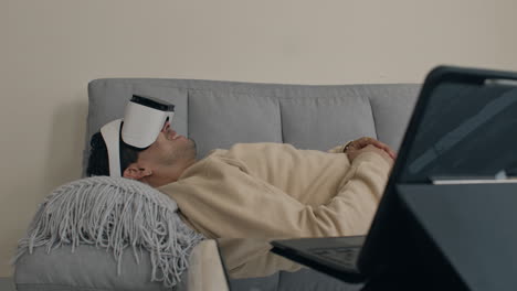 Relaxed man wearing VR headset while lounging on couch at home, immersive tech experience