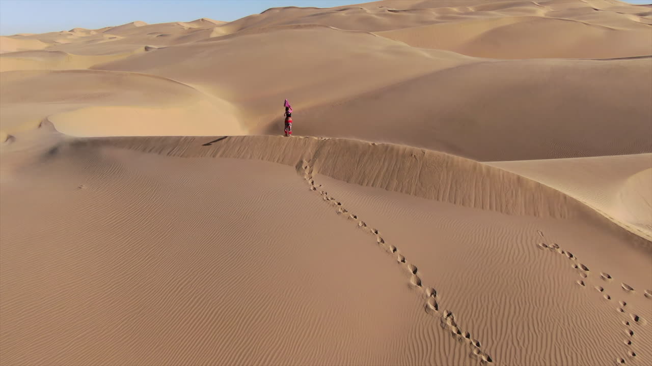Drone circling around a woman holding a blanket in the air in the Sahara desert.