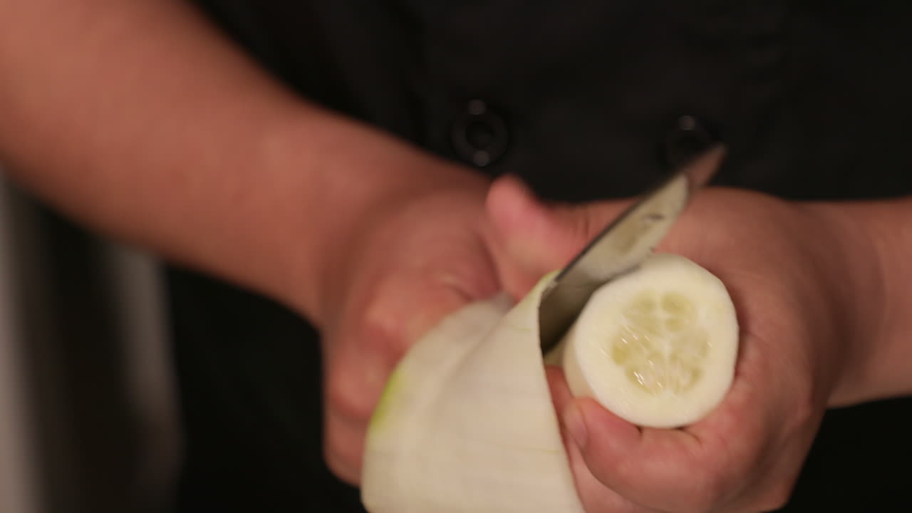 숙련된 요리사가 일본 전통 스시 롤을 위해 칼로 오이를 얇게 자른다