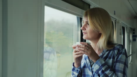 Una-Mujer-Con-Una-Taza-De-Café-Mira-Por-La-Ventana-Desde-Un-Tren