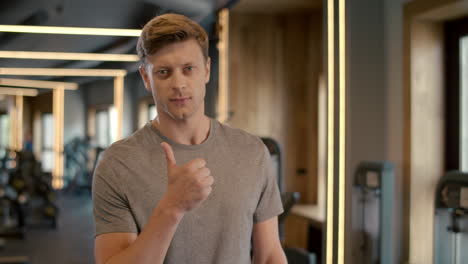 handsome fitnessman showing thumb up in sport club. sportsman standing at gym.