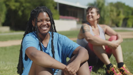 happy woman in activewear sitting on lawn and smiling at camera