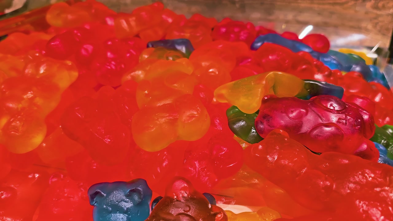 Detailansicht von verschiedenen Gummibärchen in leuchtenden Fruchtfarben, die weiche Gelatineformen, glänzende Oberflächen, geringe Tiefenschärfe und eine lebendige Großpackung Süßigkeiten für Aufnahmen aus dem Süßwarenhandel zeigt.