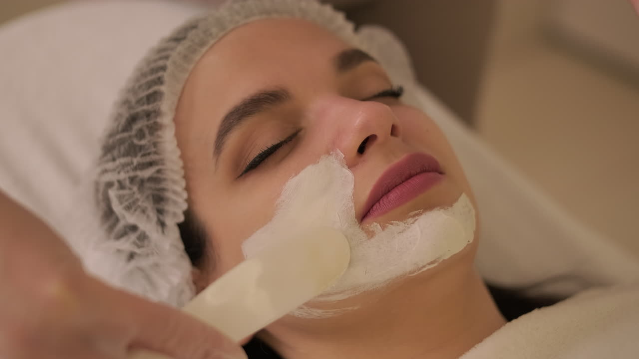 Cosmetologist Applying Facial Mask to Young Woman's Face in Spa