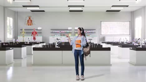 full body of asian teen girl student with a backpack and some books smiling and pointing to side while standing in science laboratory