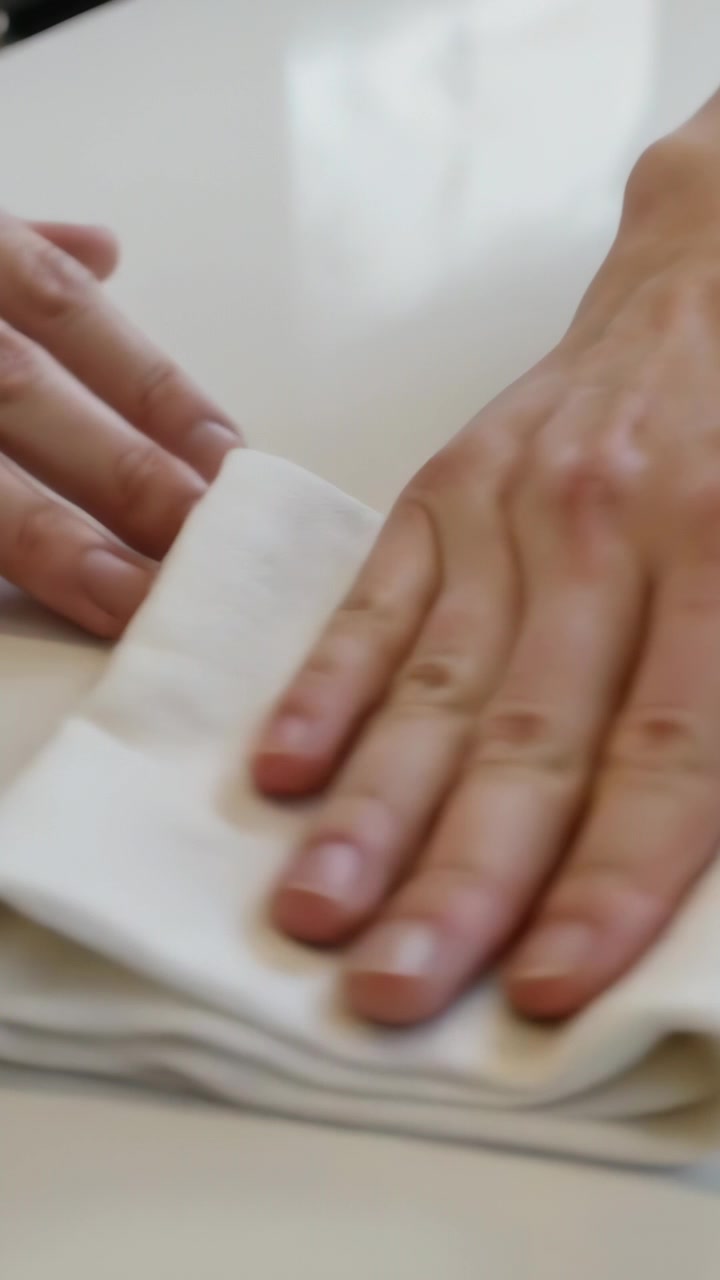 Video verticale: Mano adulta che tampona una fuoriuscita e pulisce una goccia ambrata su un tavolo da cucina con un panno