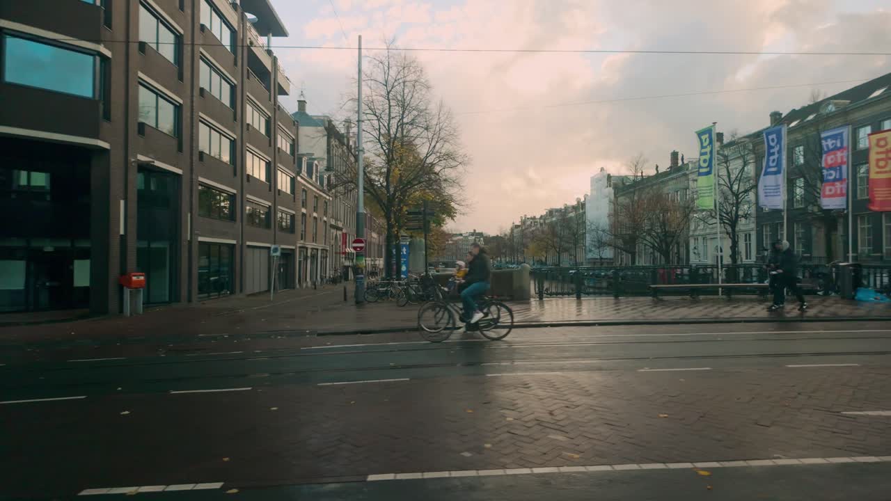 Tranquil Amsterdam street scene with tram tracks and trees, featuring a mix of modern and historic architecture on a cloudy autumn day