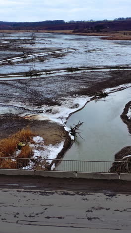 gloomy scene of nature. polluted river floating under the bridge on muddy background in springtime. ecological problems. view from above. vertical video