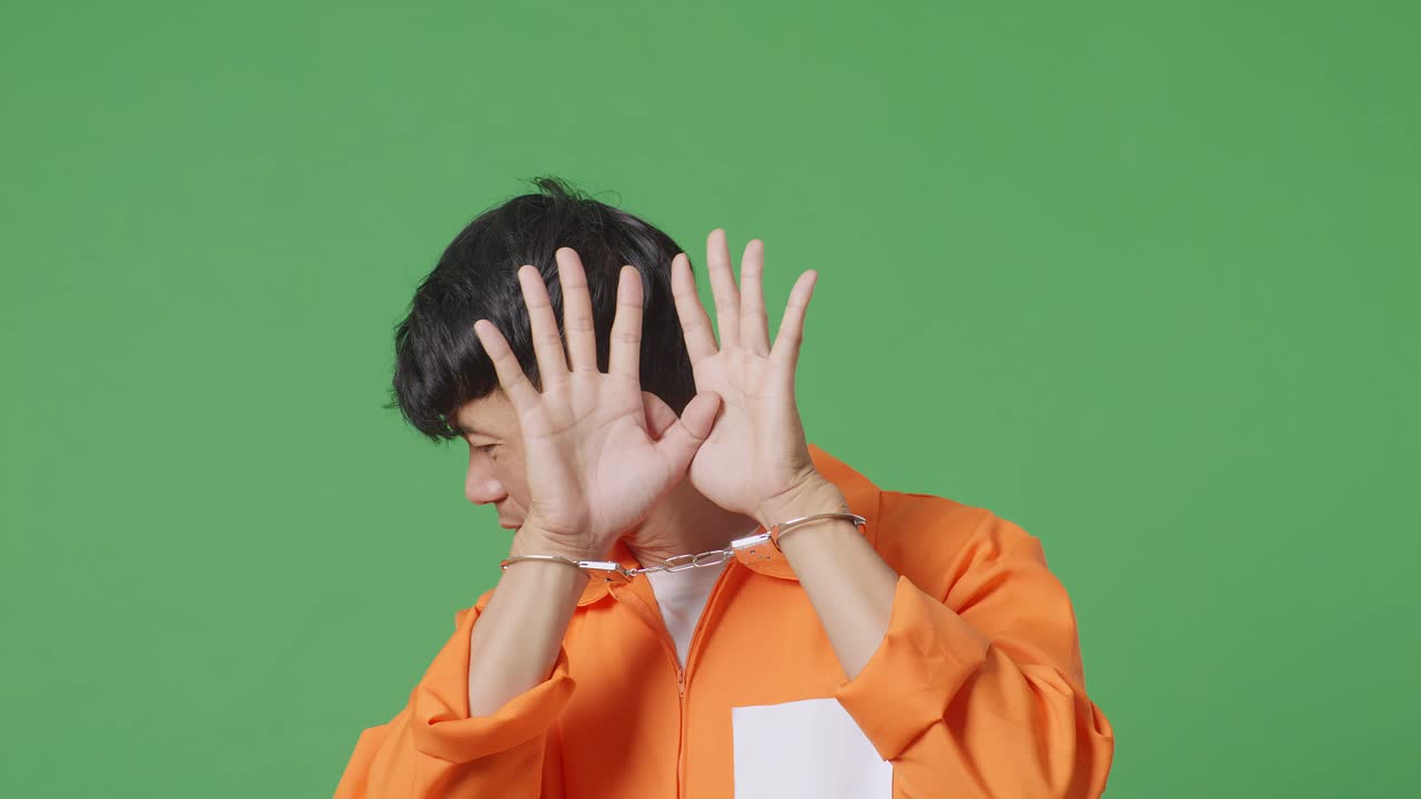 녹색 스크린 배경에 서서 손을 고 있는 아시아 남성 수감자의 클로즈업, 손바닥 표정, 카메라에 의해 포착되기를 원하지 않는 표정