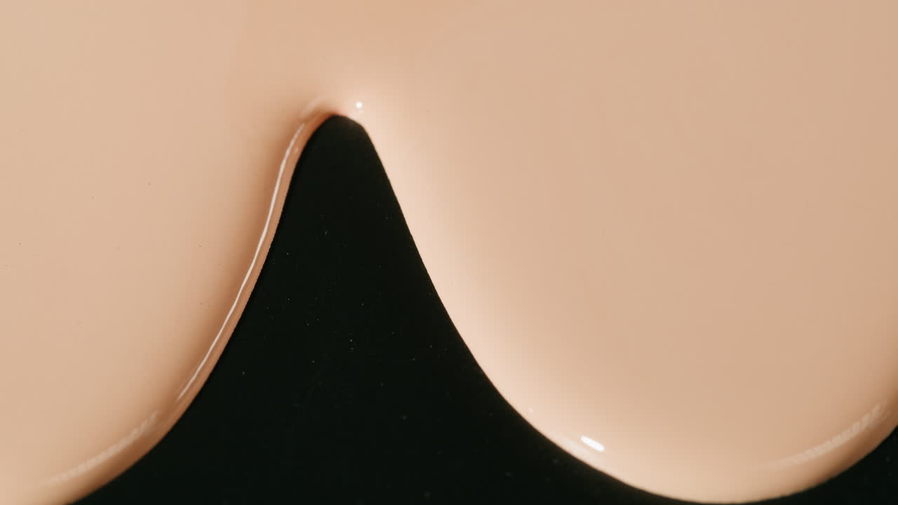 Gocce di fondotinta beige viscoso che si fondono su una superficie nera