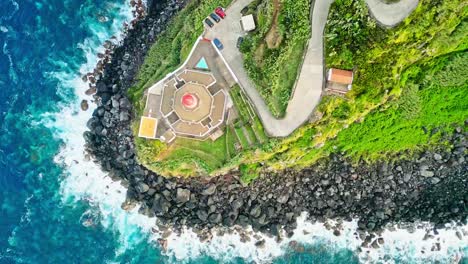 Aerial-topdown-view-of-beautiful-Arnel-lighthouse-on-rugged-headland-by-Atlantic-Ocean-waves,-Azores