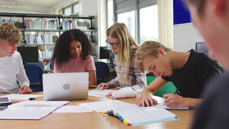 Grupo-De-Estudiantes-Universitarios-Que-Trabajan-En-La-Biblioteca-Con-Un-Portátil