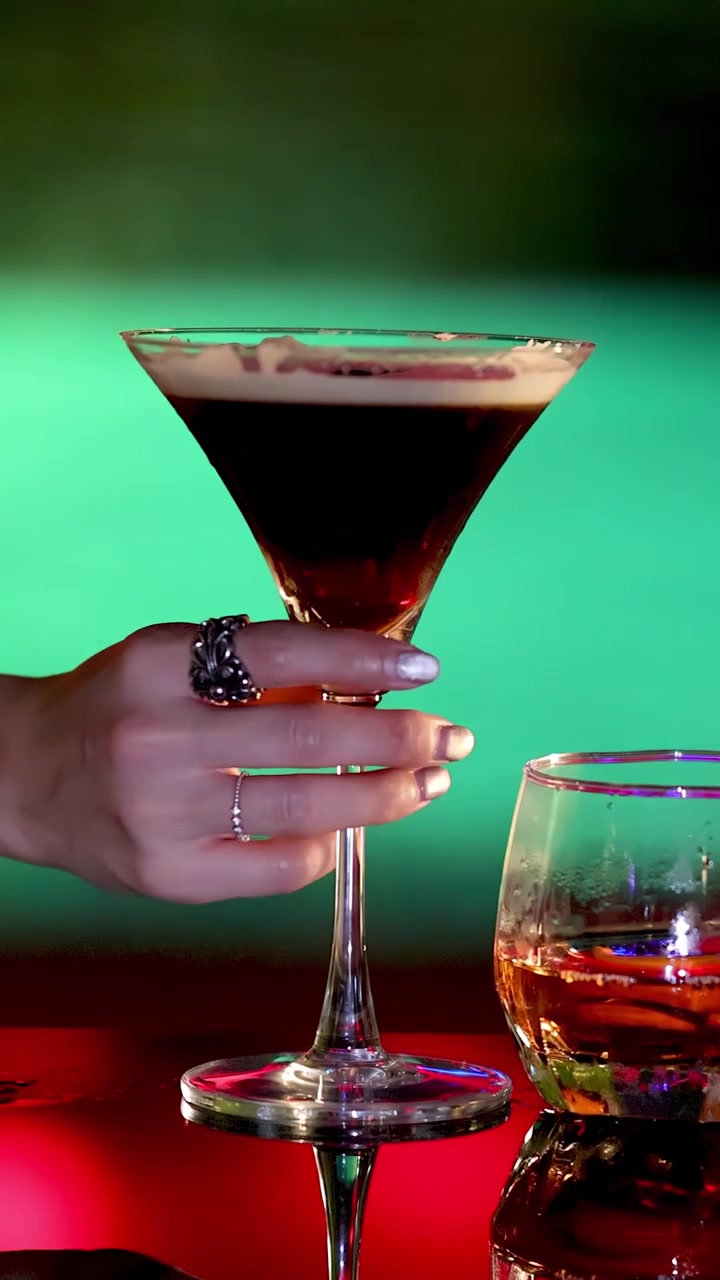 Una mano si allunga verso vari cocktail su un vivace bancone da bar, illuminazione drammatica, profondità di campo ridotta