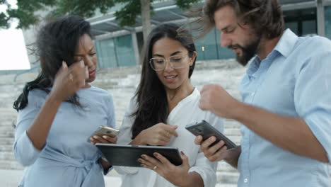 three business people standing outdoors with smartphones and tablet