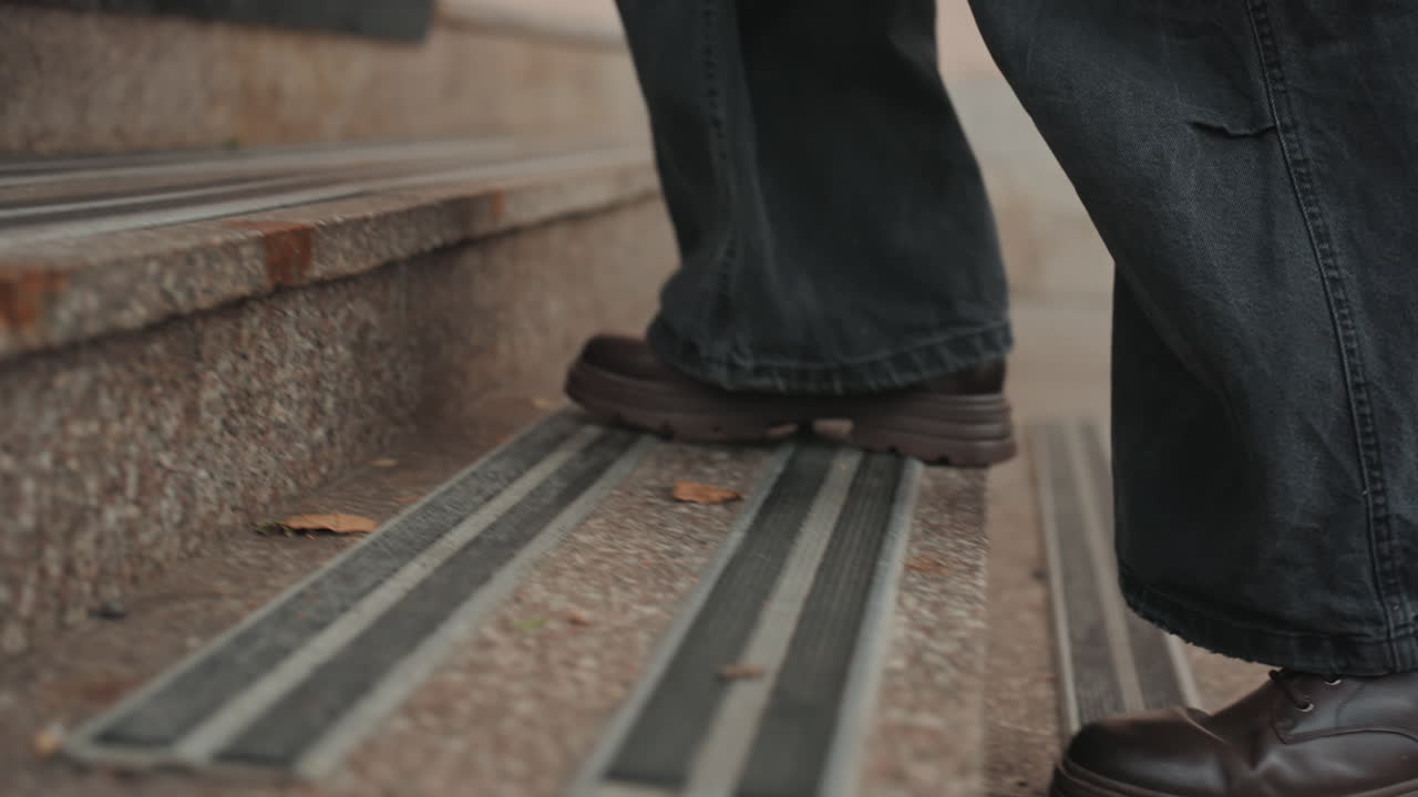 Closeup shoes stepping on entrance mat, creator arriving in jeans and worn leather shoes, moving across textured mat and granite steps toward studio doorway, lowangle candid shot, backpack blurred