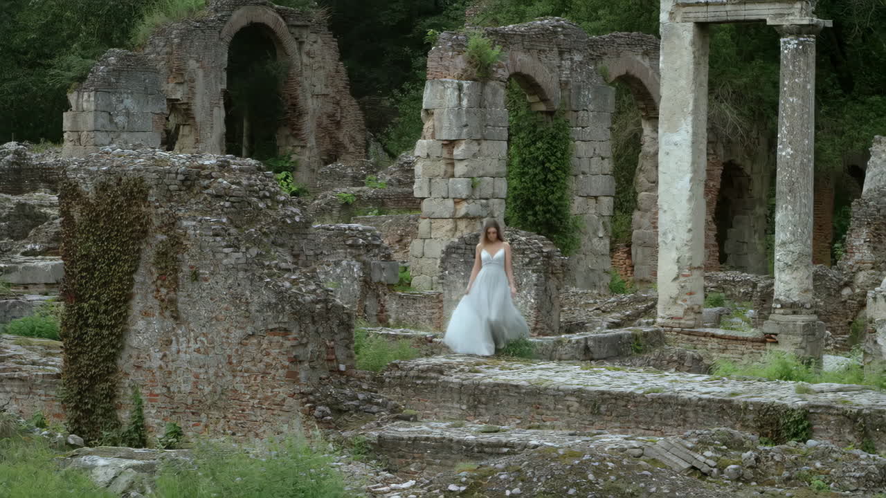 Woman in White Dress Walking Through Ancient Stone Ruins