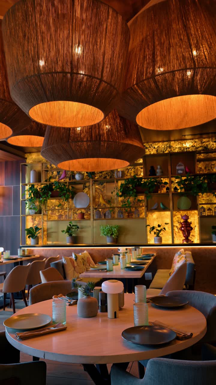 Moderne restaurantinteriør med flettede lamper og plantehylder. Udsigt over en spisestue med store flettede pendellamper og en dekorativ hylde med grønne planter.