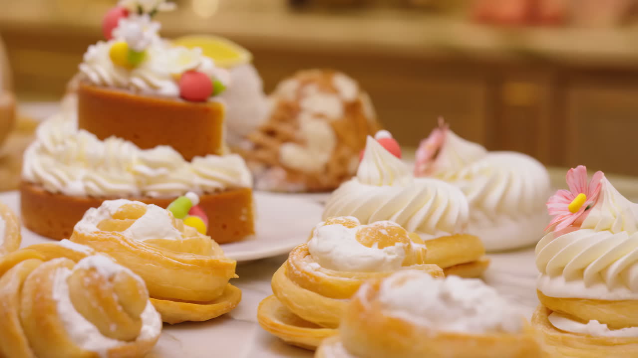 A close-up view of various delectable pastries and cakes, adorned with whipped cream and decorations, displayed on a table
