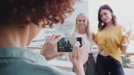 Young-woman-taking-photos-with-smartphone-of-girlfriends-drinking-on-a-balcony-in-the-city,-close-up