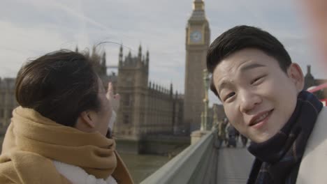 young asian couple on holiday making video call home on phone at houses of parliament in london uk