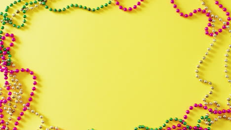 video of pink, gold and green mardi gras carnival beads on yellow background with copy space