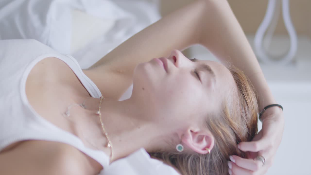 매력적인 젊은 여성이 머리카락을 만지고 침대에서 휴식을 취하고 있습니다.