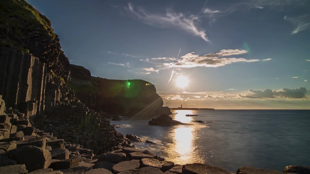 Colunas de basalto e rochas hexagonais iluminadas na costa, sol nascente criando reflexo quente, espaço para texto