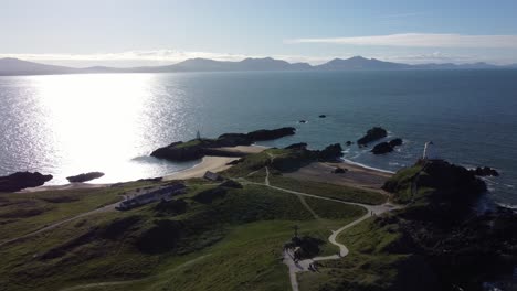 aerial view ynys llanddwyn welsh island beach with shimmering ocean and misty snowdonia mountain range across the sunrise skyline