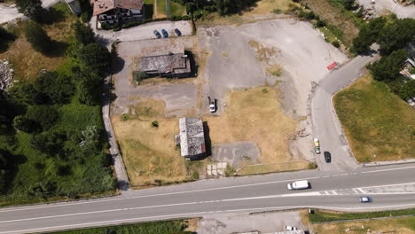 vista de arriba hacia abajo sobre un área abandonada en la montaña cerca de la carretera principal con vehículos que pasan en morgex, val d'aosta, italia - toma aérea de drones