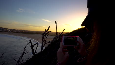 woman silhouetted against sunset taking photo of beach