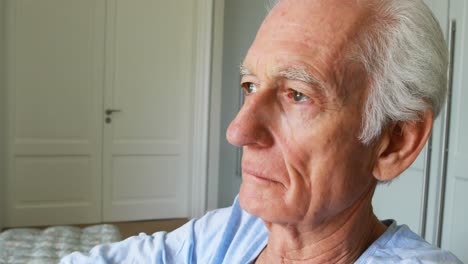 senior man sitting in wheelchair looking through window in bedroom