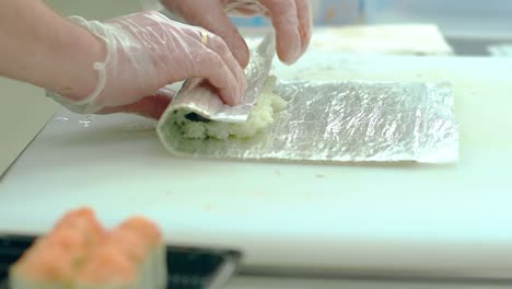 cook prepares japanese sushi with prawns rice and nori seaweed using a mat