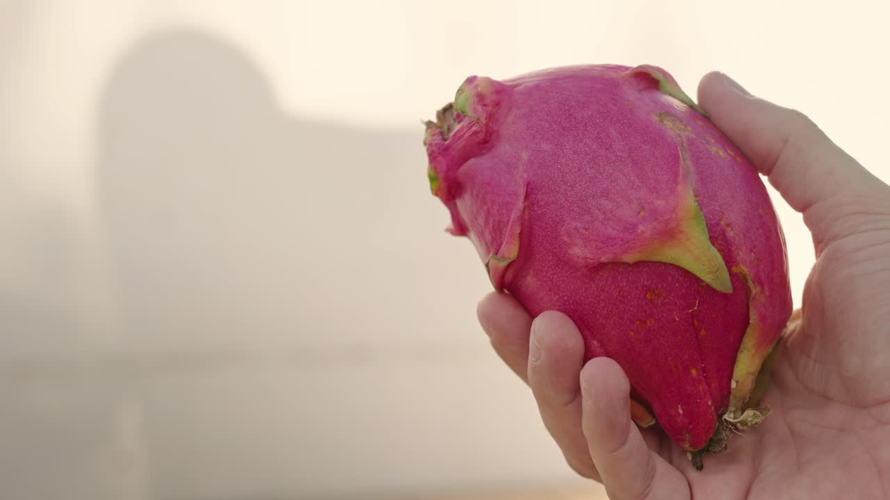 Dragon fruit in man's hand moving over white background golden hour