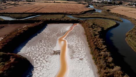 Salinas-Para-La-Producción-De-Sal-Junto-A-Un-Río-Entre-Campos,-Drone-Dolly-Lejos