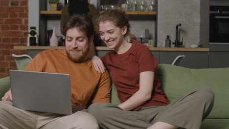 girl and boy watching videos with laptop while their female roommate cleaning the house