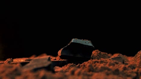 Slow-motion-close-up-shot-of-falling-chocolate-pieces-in-cocoa-while-the-ground-rotates-against-a-black-background