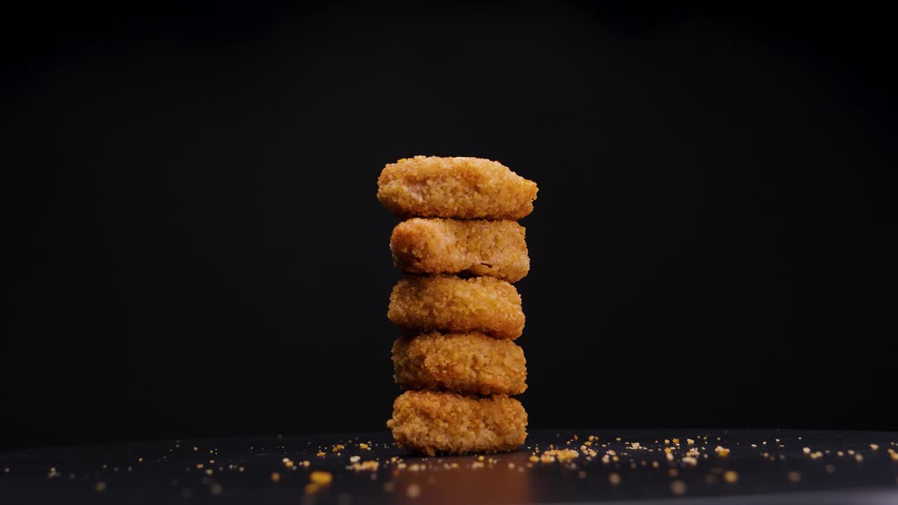 pila de nuggets de pollo vegetarianos, marrones dorados, bellamente cocinados, girando sobre un fondo negro, tiro estático
