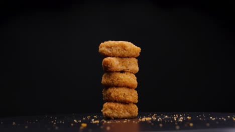 stack of beautifully cooked vegetarian, golden brown chicken nuggets rotating against a black background, static shot