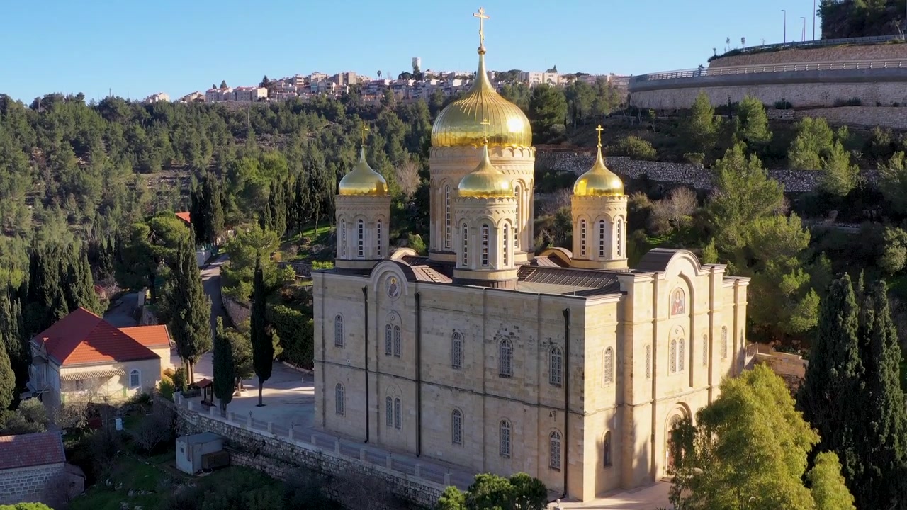 Filmagem de drone em ângulo alto mostrando as cúpulas douradas do Convento Ortodoxo Russo Gorny cercado por colinas verdes em Ein Karem.