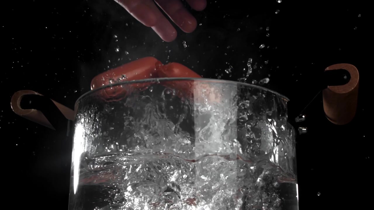 Salsicce che cadono in acqua bollente in una pentola trasparente