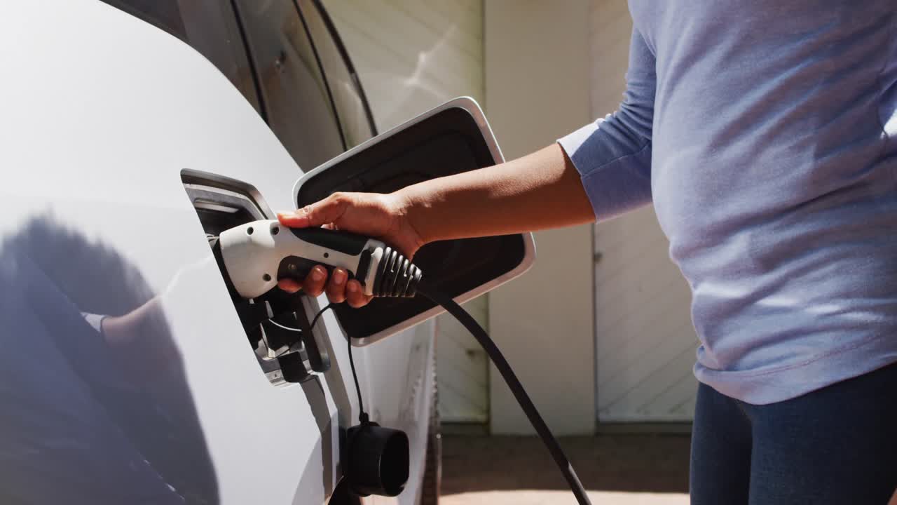 sección media de una mujer afroamericana cargando un coche eléctrico en un día soleado