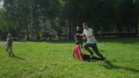 la familia disfruta de un animado juego de fútbol al aire libre mientras ambos chicos persiguen la pelota con determinación mientras el hermano de rojo patea la pelota a través del campo cubierto de hierba en un día soleado.