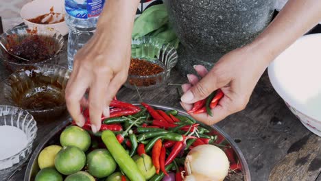 Hands-removing-stalks-from-chili-peppers-on-table-of-ingredients