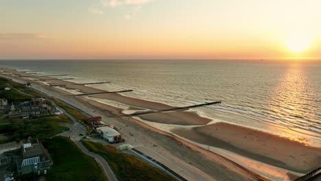 Beautiful-aerial-shot-of-a-beach-with-wooden-groins-to-prevent-erosion,-at-high-tide-during-sunset