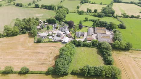 Drone-exterior-view-of-a-smallholding-farming-community-in-Devon,-UK,-showcasing-farm-buildings,-fields,-and-rural-surroundings